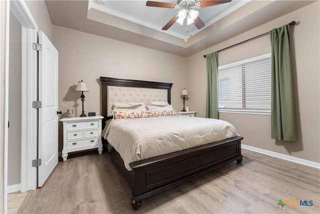 bedroom featuring ornamental molding, wood finished floors, baseboards, a raised ceiling, and a ceiling fan