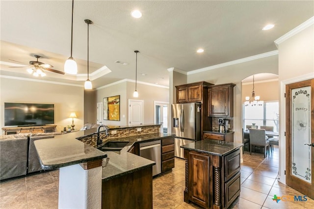 kitchen with dark stone countertops, a spacious island, arched walkways, a sink, and appliances with stainless steel finishes