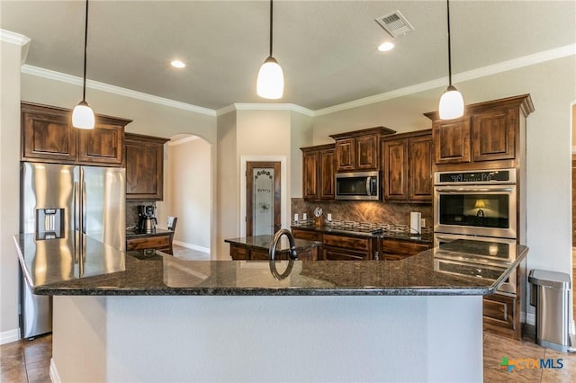 kitchen featuring visible vents, tasteful backsplash, stainless steel appliances, arched walkways, and a large island with sink