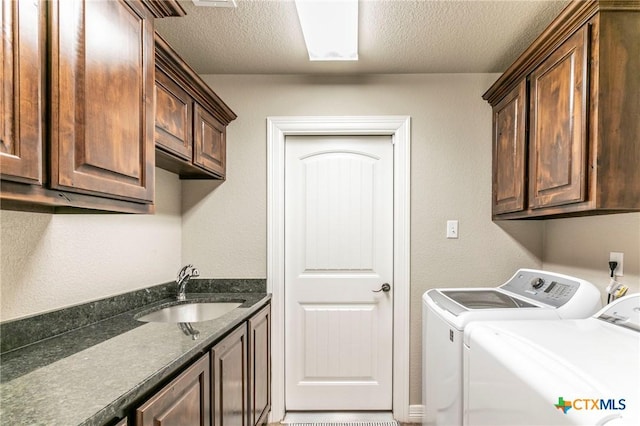 washroom with a sink, cabinet space, a textured ceiling, and washing machine and clothes dryer