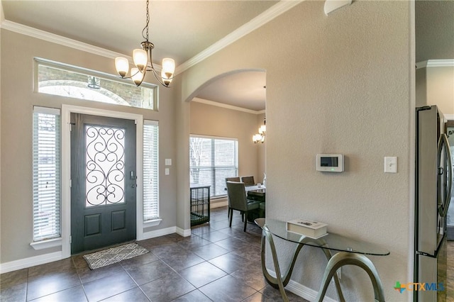 foyer featuring baseboards, an inviting chandelier, arched walkways, crown molding, and dark tile patterned floors