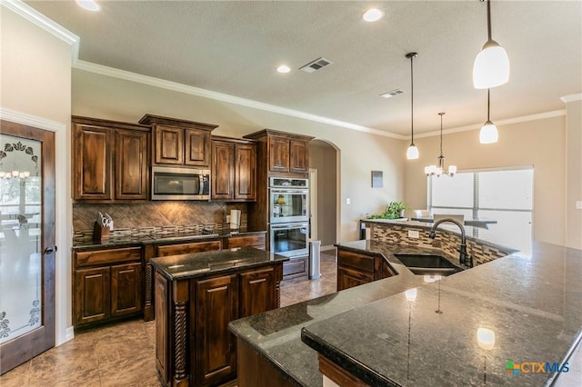 kitchen with a spacious island, visible vents, arched walkways, stainless steel appliances, and a sink