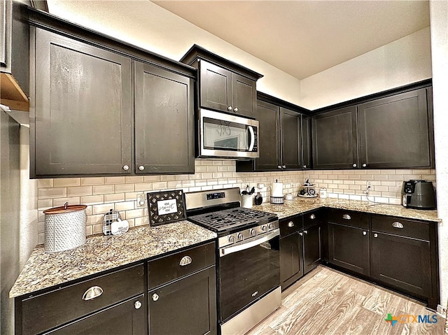 kitchen with light stone countertops, appliances with stainless steel finishes, tasteful backsplash, and light hardwood / wood-style flooring