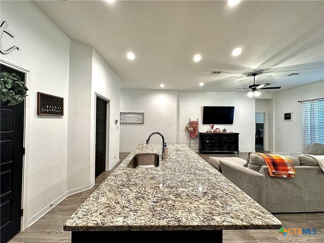 kitchen featuring light stone counters, a center island with sink, and sink