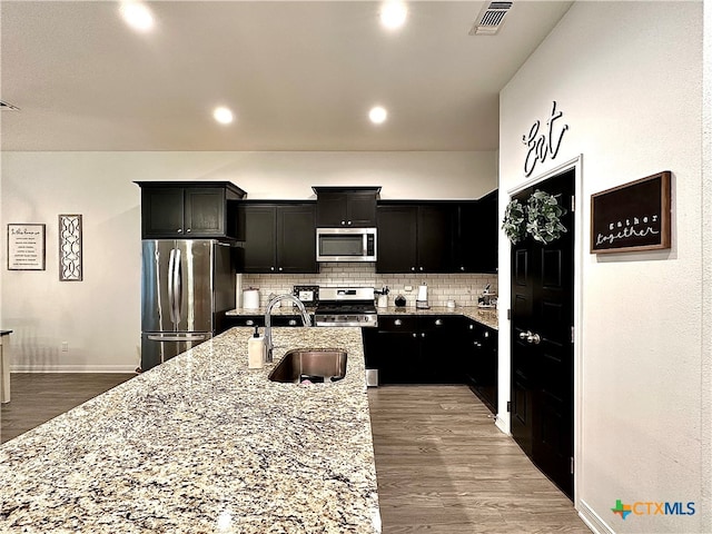 kitchen with stainless steel appliances, sink, backsplash, wood-type flooring, and a kitchen island with sink