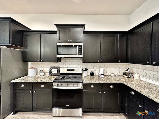 kitchen featuring decorative backsplash, appliances with stainless steel finishes, light hardwood / wood-style floors, and light stone counters