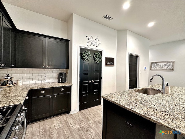 kitchen with decorative backsplash, light hardwood / wood-style floors, sink, and light stone counters