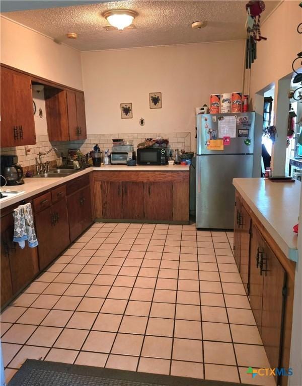 kitchen featuring a textured ceiling, black microwave, light countertops, a sink, and freestanding refrigerator