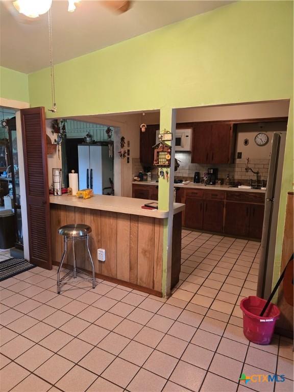 kitchen featuring white appliances, light countertops, a peninsula, decorative backsplash, and light tile patterned floors