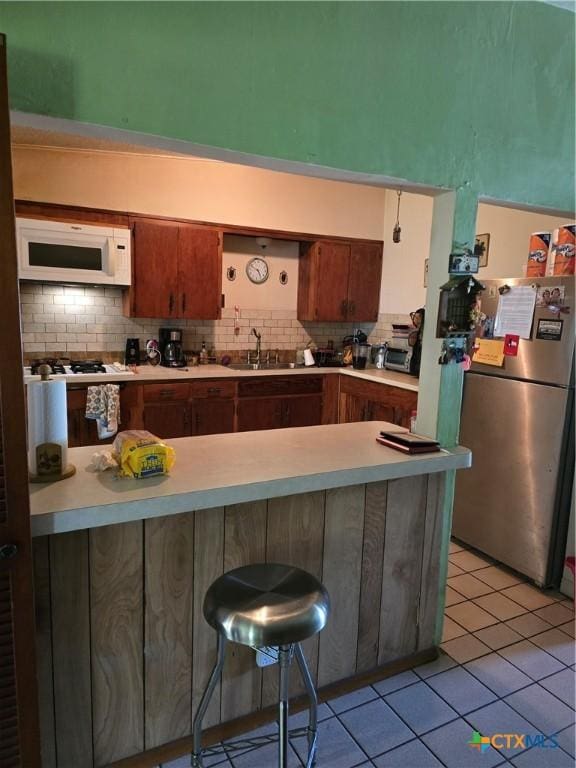 kitchen featuring freestanding refrigerator, a peninsula, white microwave, a sink, and backsplash