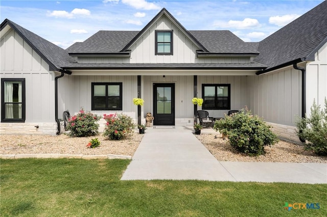 view of front of home featuring covered porch, board and batten siding, a front lawn, and roof with shingles