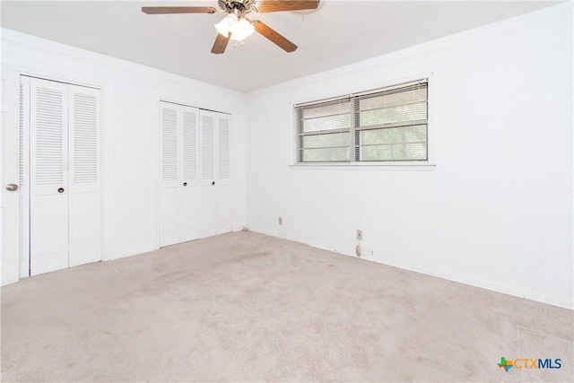 unfurnished bedroom featuring two closets, ceiling fan, crown molding, and carpet