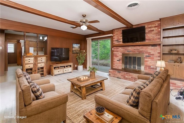 living room with ceiling fan, wooden walls, a fireplace, beam ceiling, and light hardwood / wood-style flooring