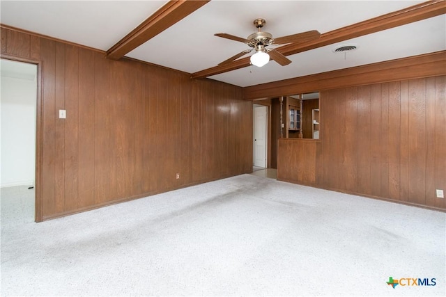 carpeted spare room with ceiling fan, wooden walls, and beamed ceiling