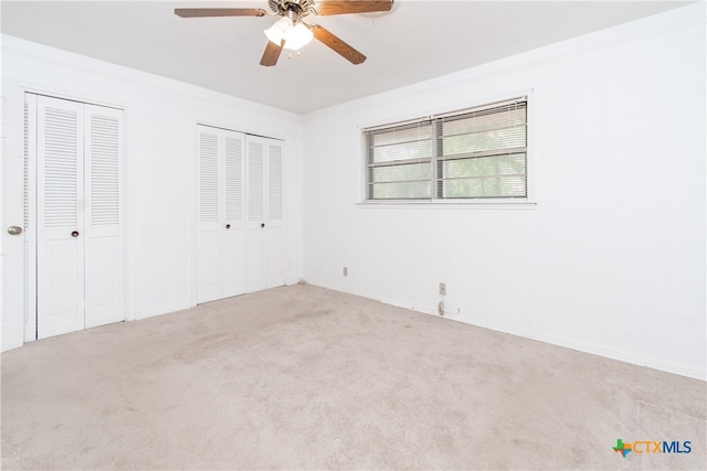 unfurnished bedroom featuring ceiling fan, light colored carpet, two closets, and crown molding