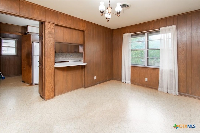 kitchen with white refrigerator, decorative light fixtures, wood walls, and a notable chandelier