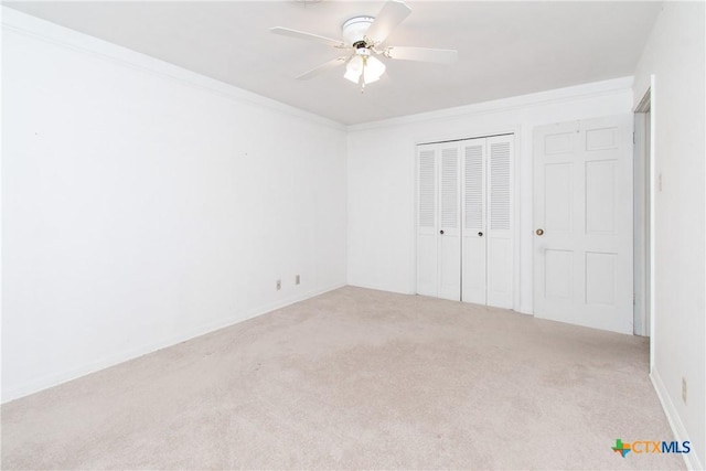 unfurnished bedroom with ornamental molding, ceiling fan, a closet, and light carpet