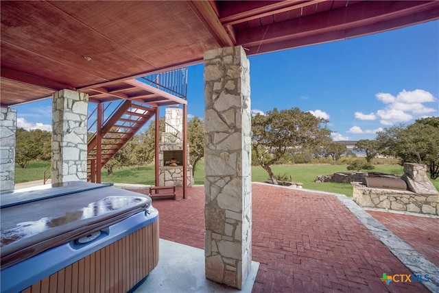 view of patio with an outdoor stone fireplace and a hot tub