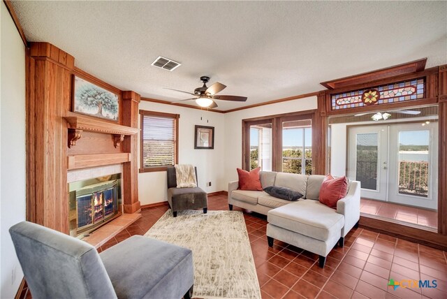 living room with a tile fireplace, french doors, ceiling fan, ornamental molding, and a textured ceiling