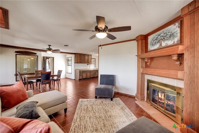 living room featuring a tiled fireplace, crown molding, tile patterned flooring, and ceiling fan