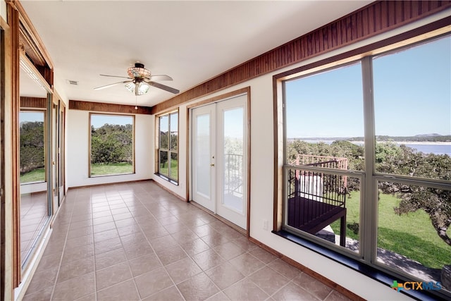 unfurnished sunroom with ceiling fan, a water view, and french doors