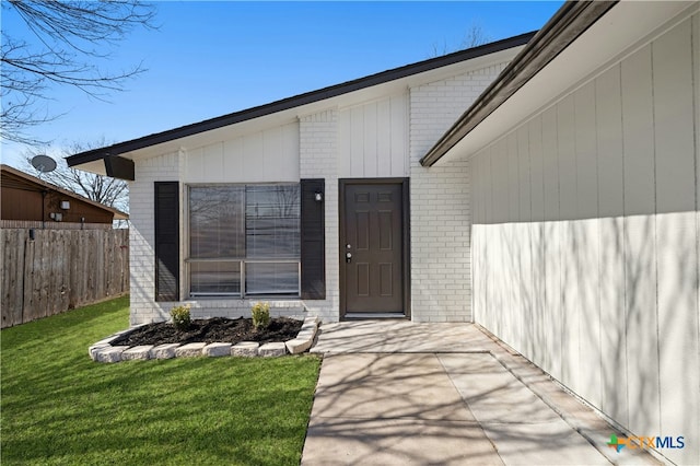 view of exterior entry featuring brick siding, fence, and a yard