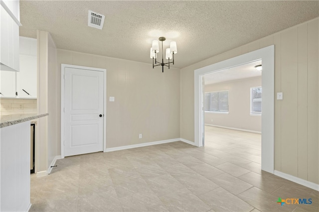 unfurnished dining area featuring an inviting chandelier, baseboards, visible vents, and a textured ceiling