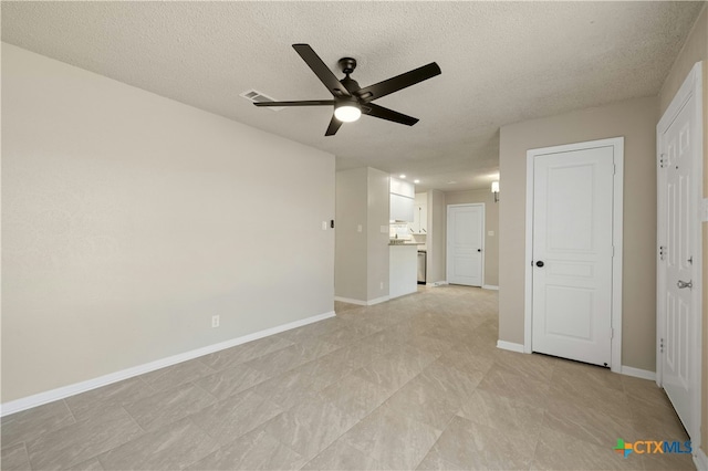 empty room with ceiling fan, a textured ceiling, visible vents, and baseboards