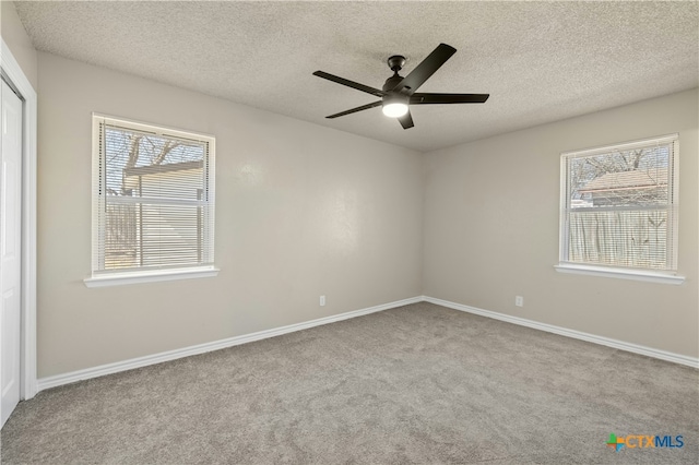 spare room featuring a textured ceiling, a ceiling fan, a wealth of natural light, and carpet flooring