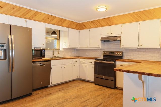 kitchen with stainless steel appliances, under cabinet range hood, a sink, tasteful backsplash, and butcher block countertops