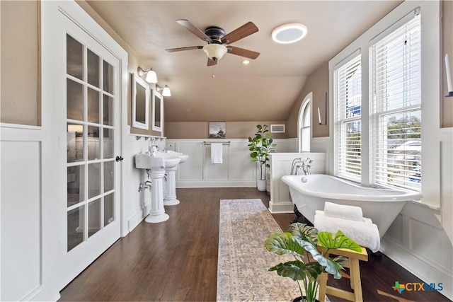 bathroom with a wainscoted wall, lofted ceiling, a freestanding bath, a ceiling fan, and wood finished floors