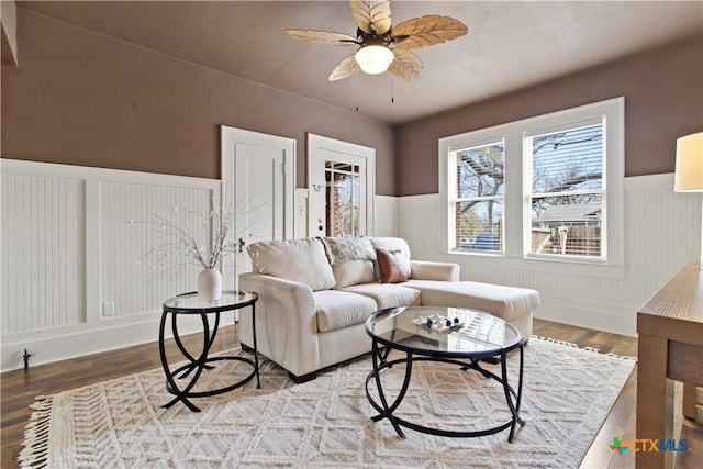 living area featuring light wood-style floors, ceiling fan, and a wainscoted wall