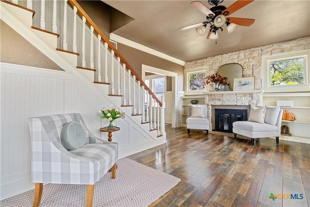 sitting room with a fireplace, wood-type flooring, stairway, wainscoting, and ceiling fan