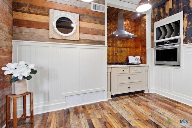 kitchen featuring black gas cooktop, hardwood / wood-style flooring, oven, visible vents, and wall chimney exhaust hood