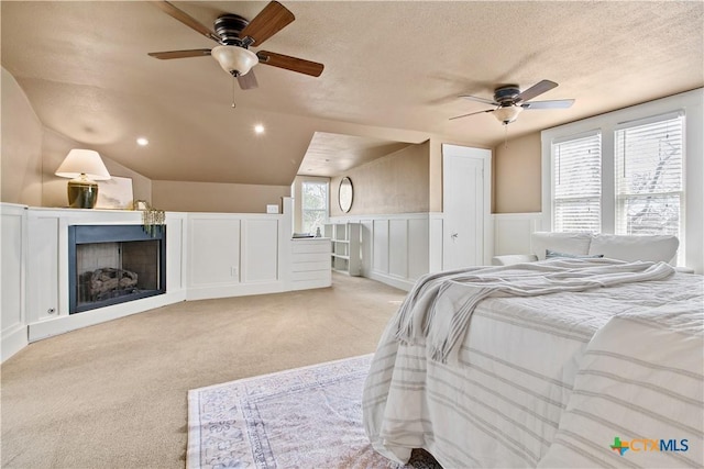 bedroom featuring a textured ceiling, lofted ceiling, light colored carpet, a fireplace, and wainscoting