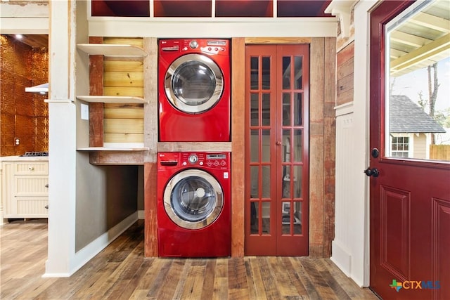 clothes washing area featuring stacked washer and dryer, wood finished floors, laundry area, and baseboards