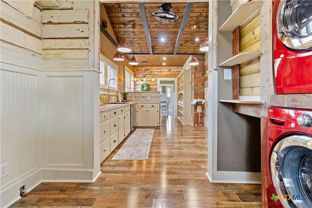 laundry area featuring stacked washer and dryer, wooden ceiling, a sink, wood finished floors, and laundry area