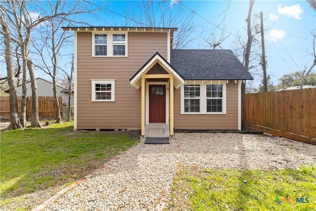 traditional home with a shingled roof, fence, and a front yard