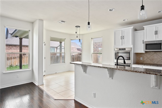 kitchen with a kitchen bar, hardwood / wood-style floors, hanging light fixtures, white cabinetry, and appliances with stainless steel finishes