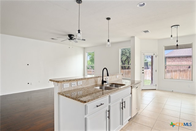 kitchen with light stone counters, white cabinets, sink, a kitchen island with sink, and light wood-type flooring