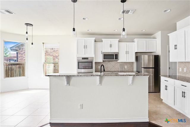 kitchen with dark stone counters, appliances with stainless steel finishes, decorative light fixtures, and a center island with sink