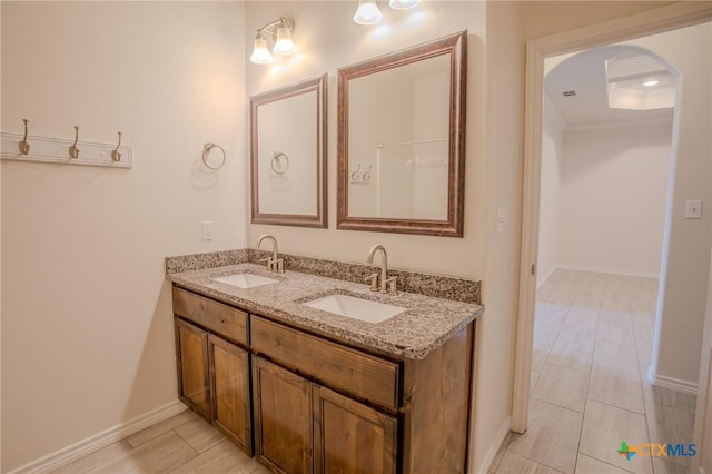 full bath with baseboards, double vanity, and a sink