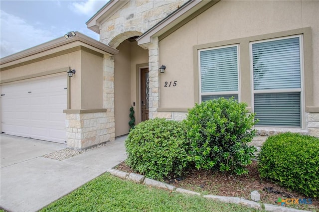 property entrance featuring stucco siding, driveway, an attached garage, and stone siding