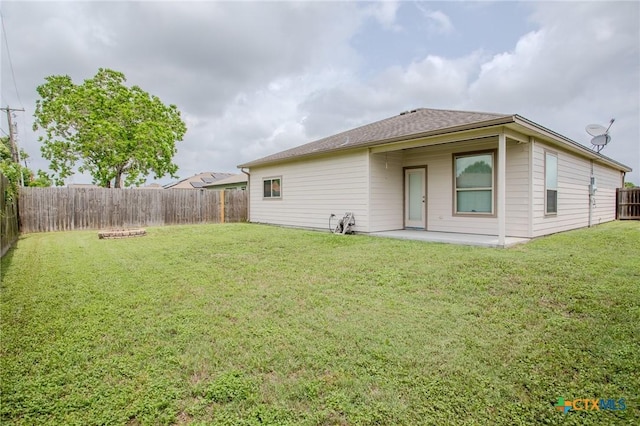 rear view of property featuring roof with shingles, a yard, a patio, and a fenced backyard