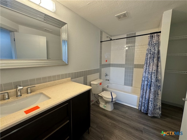 full bathroom with a textured ceiling, hardwood / wood-style floors, shower / tub combo with curtain, toilet, and tile walls