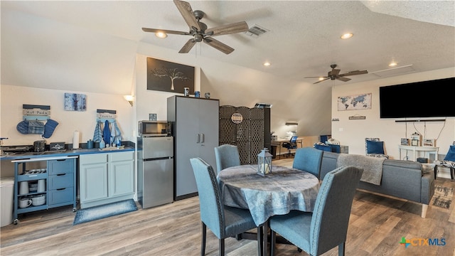 dining room featuring ceiling fan, lofted ceiling, a textured ceiling, and light hardwood / wood-style flooring