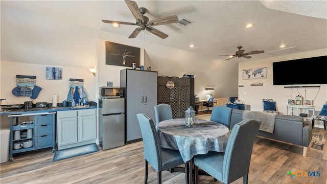 dining space with ceiling fan, lofted ceiling, light hardwood / wood-style flooring, and a textured ceiling