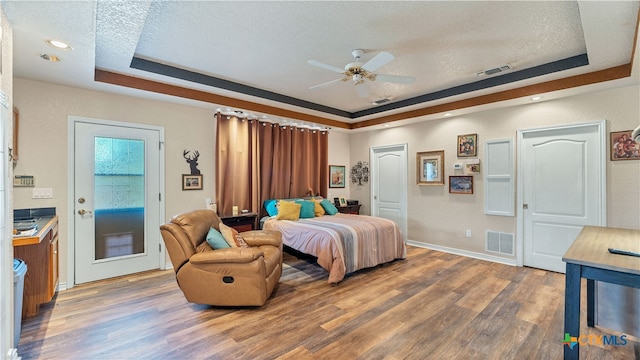 bedroom with dark wood-type flooring, ceiling fan, a tray ceiling, a textured ceiling, and access to outside