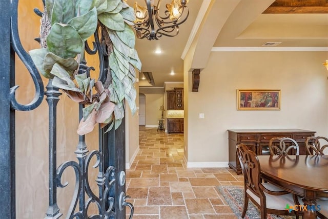 interior space with stone tile floors, an inviting chandelier, baseboards, ornamental molding, and visible vents
