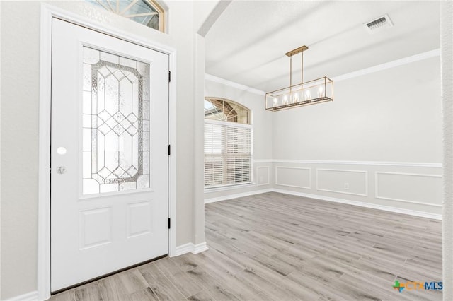 foyer entrance featuring ornamental molding, a chandelier, and light wood-type flooring